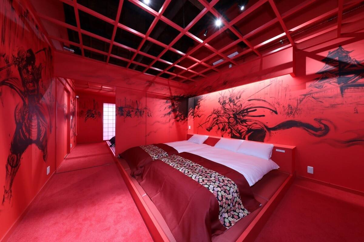 A room with a bed, red walls, and artwork.