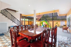 A spacious dining area with a large wooden table and red upholstered chairs, a staircase, and a colorful play area in the background. - 99 Pool Villa (Pattaya)