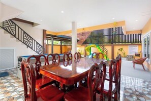 A spacious dining area with a large wooden table and matching chairs, a staircase, and a vibrant wall mural. - 99 Pool Villa (Pattaya)