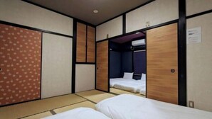 Une chambre de style japonais traditionnel, avec un sol recouvert de tatamis, deux lits simples, une armoire et une porte coulissante.