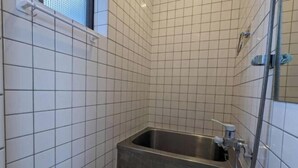 Une petite salle de bain carrelée, équipée d’une douche, d’un lavabo et de toilettes.