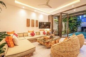A modern living room with a sofa, a glass coffee table, and wicker chairs. - Villa Chili in Dalung (Bali)