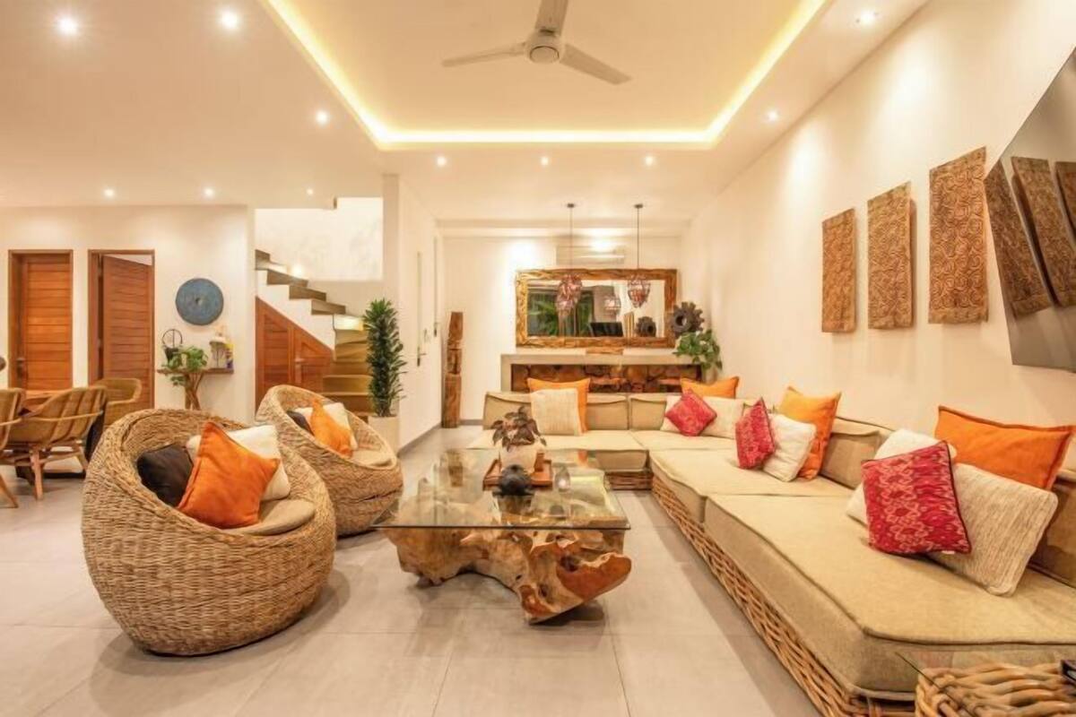 A modern living room with a sofa, two wicker chairs, a glass coffee table, and a staircase leading to another level.