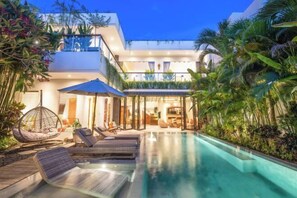 A modern pool area with lounge chairs and a hanging chair, surrounded by lush tropical plants. - Villa Chili in Dalung (Bali)