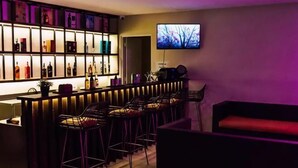 A bar area with a TV mounted on the wall, a shelf with bottles, and a seating area with a red couch. - The First Islatel (Alaminos)