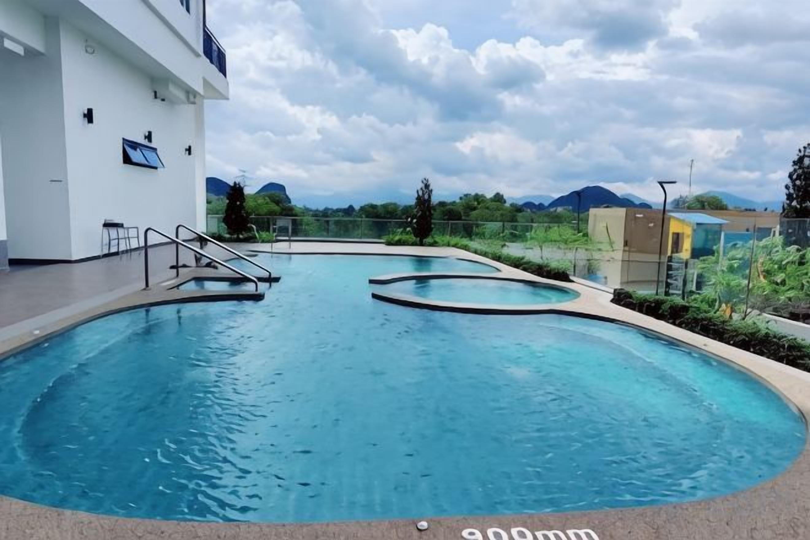 Une piscine avec vue sur les montagnes, un bâtiment doté d’un balcon et un ciel dégagé.