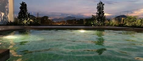 A swimming pool with clear water, surrounded by greenery and a white building.