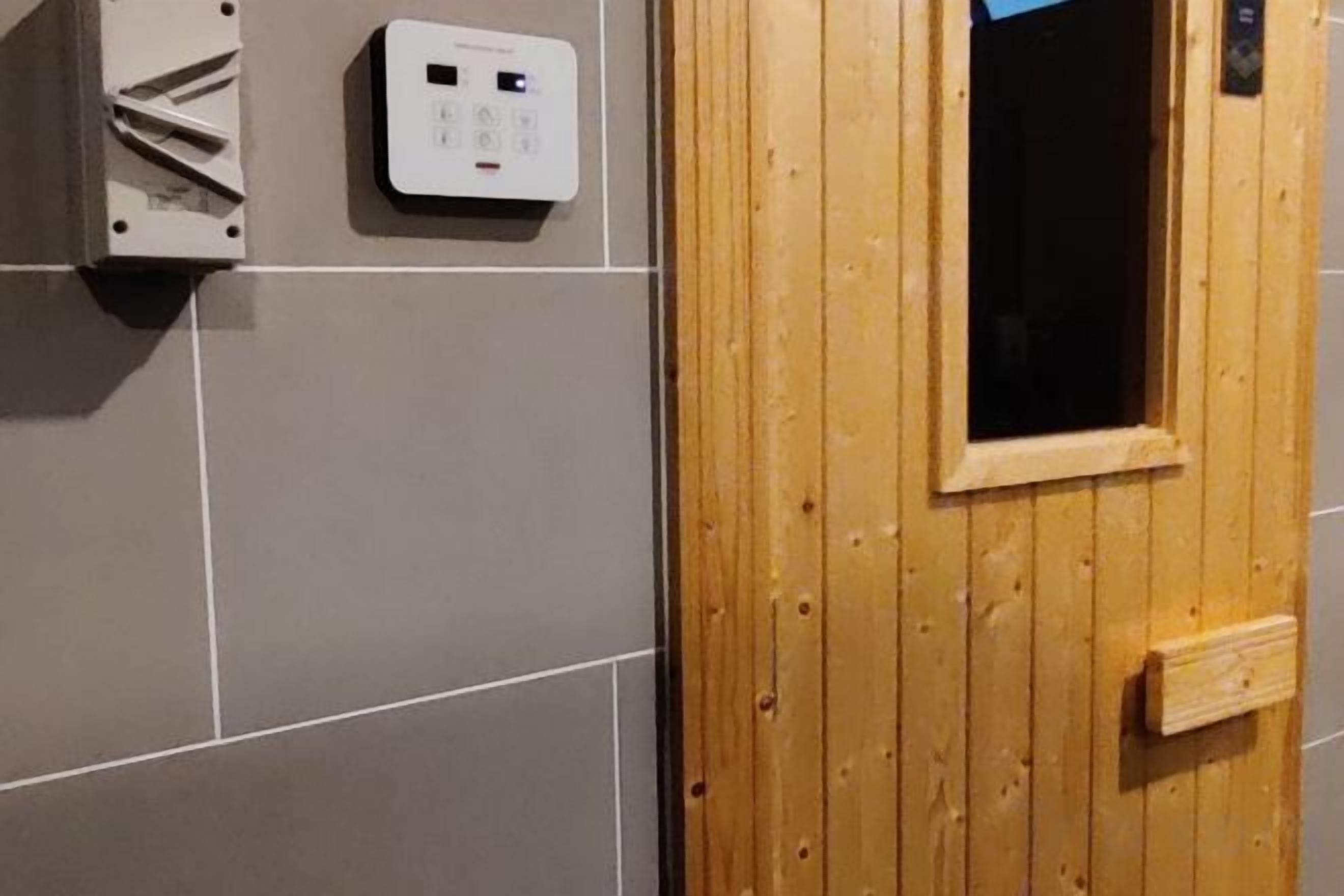 A wooden door with a window, a wall-mounted electrical box, and grey tiles.