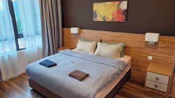 A hotel room with a large bed, bedside tables, a nightstand, and a window with curtains.