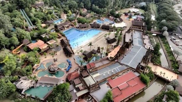 Vista aérea de un complejo turístico con una gran piscina, varias toboganes acuáticos y diferentes edificios.