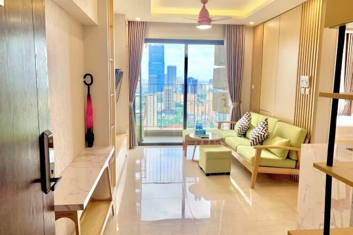 Una sala de estar moderna con un sofá, una mesa de centro y vistas de un paisaje urbano a través de amplios ventanales.