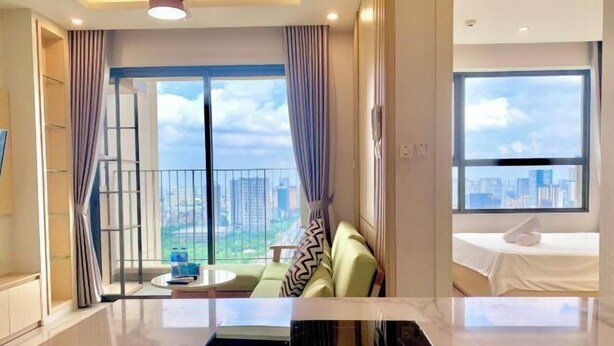 A modern hotel room with a balcony, a sofa, a bed, and a view of the cityscape. - LukaHomes - Dcapitale/1BR+/City view (Hanoi)