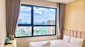 A hotel room with a large window offering a cityscape view, a neatly made bed, and a bedside table with a lamp. - LukaHomes - Dcapitale/1BR+/City view (Hanoi)
