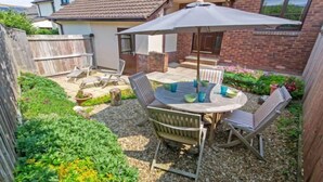 A backyard with a patio table, chairs, and a large umbrella. - Cockleshell Croyde Sleeps 4 By the Seaside (Croyde)