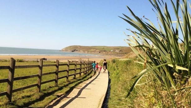 A coastal path with a wooden fence, a paved walkway, and a grassy area with a plant on the right. - Cockleshell Croyde Sleeps 4 By the Seaside (Croyde)