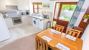 A compact kitchen with a dining area, a washing machine, and a small dining table with chairs. - Cockleshell Croyde Sleeps 4 By the Seaside (Croyde)