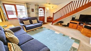A living room with a sofa, a television, a staircase, and a window. - Cockleshell Croyde Sleeps 4 By the Seaside (Croyde)