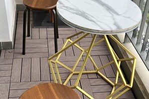 Une table ronde dotée d’un plateau en marbre et d’un socle doré aux motifs géométriques, posée sur un plancher en bois à motifs rayés.