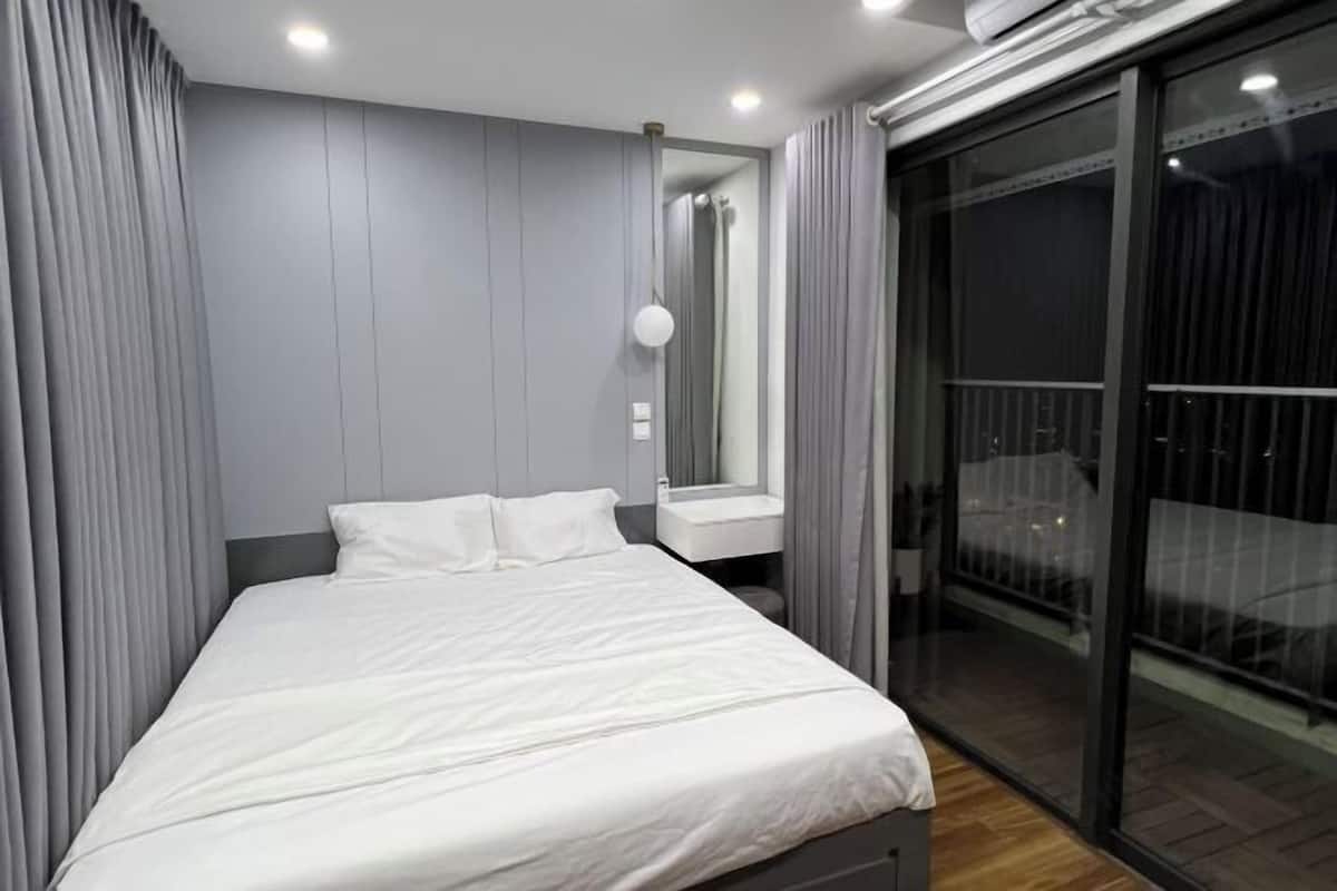 Un dormitorio moderno con cama, mesita de noche, espejo y puerta corrediza de vidrio a un balcón.