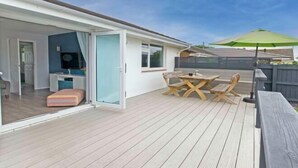 Ein überdachter Außenbereich mit Holzdeck, einem Tisch und Stühlen sowie einem grünen Sonnenschirm.