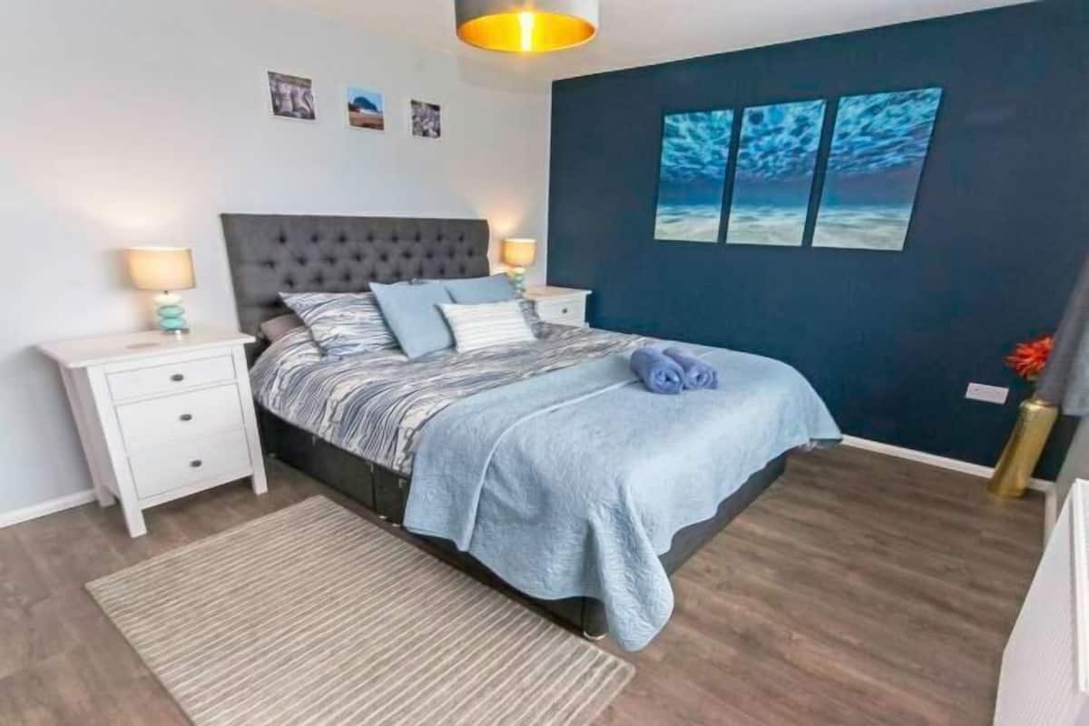Ein Schlafzimmer mit Bett, Nachttischen, Teppich und Bildern an der Wand.