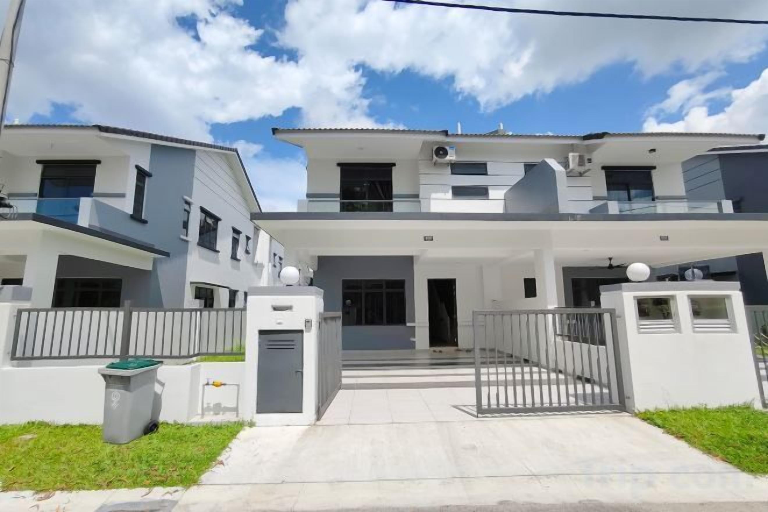 Un edificio residencial moderno de dos pisos con entrada protegida por un portón, un pequeño jardín delantero y un cielo despejado.