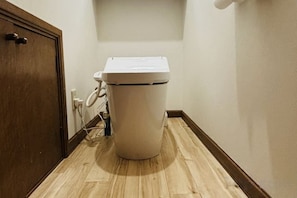 A toilet in a bathroom with a wooden door and a light switch on the wall. - 2-floor house with garden (Otaru)