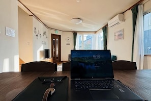 A laptop on a table in a room with a wooden floor, a door, and a window with curtains.