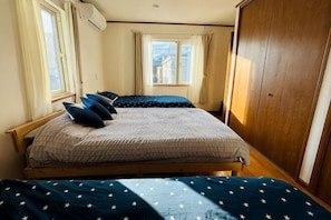 Een slaapkamer met een bed, twee ramen, een kledingkast en uitzicht op gebouwen.