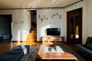 A modern living room with a sofa, coffee table, TV, and hanging light fixtures. - 2-floor house with garden (Otaru)