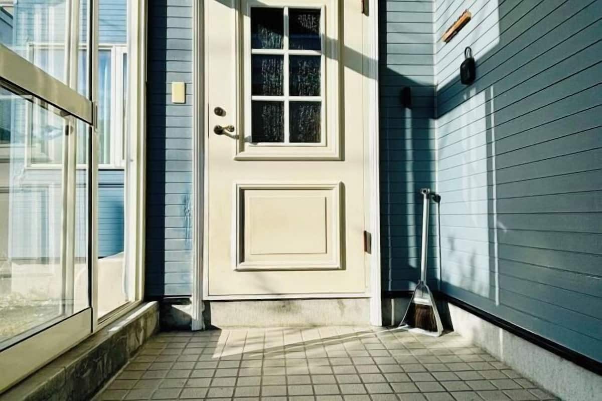 A house entrance with a white door, a window, and a broom leaning against the wall.