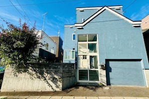 A two-story residential building with a garage, a front door, and a small porch area. - 2-floor house with garden (Otaru)