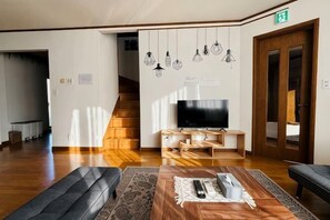 A living room with a wooden bench, a TV, and hanging light fixtures. - 2-floor house with garden (Otaru)
