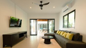A modern living room with a dark sofa, a coffee table, a TV mounted on the wall, and a ceiling fan. - Samui Paradise Poolside Villa (Koh Samui)