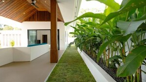 A modern interior with a wooden ceiling, a white wall with a planter, and a green artificial grass area. - Samui Paradise Poolside Villa (Koh Samui)