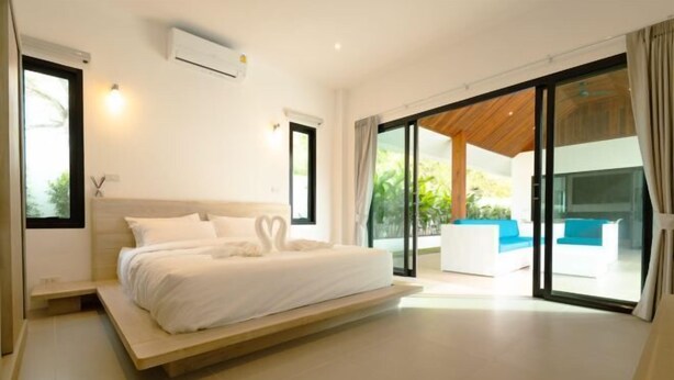A modern bedroom with a large bed, sliding glass doors to a balcony, and a built-in air conditioning unit. - Samui Paradise Poolside Villa (Koh Samui)