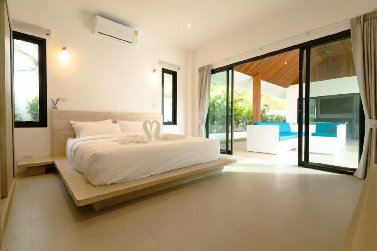 A modern bedroom with a large bed, sliding glass doors to a balcony, and a built-in air conditioning unit.