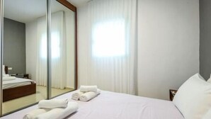 A hotel room with a bed, a large mirror, a nightstand, and a window with curtains. - Elegant Sea-View Apt w Mamad by Sea N' Rent (Tel Aviv)