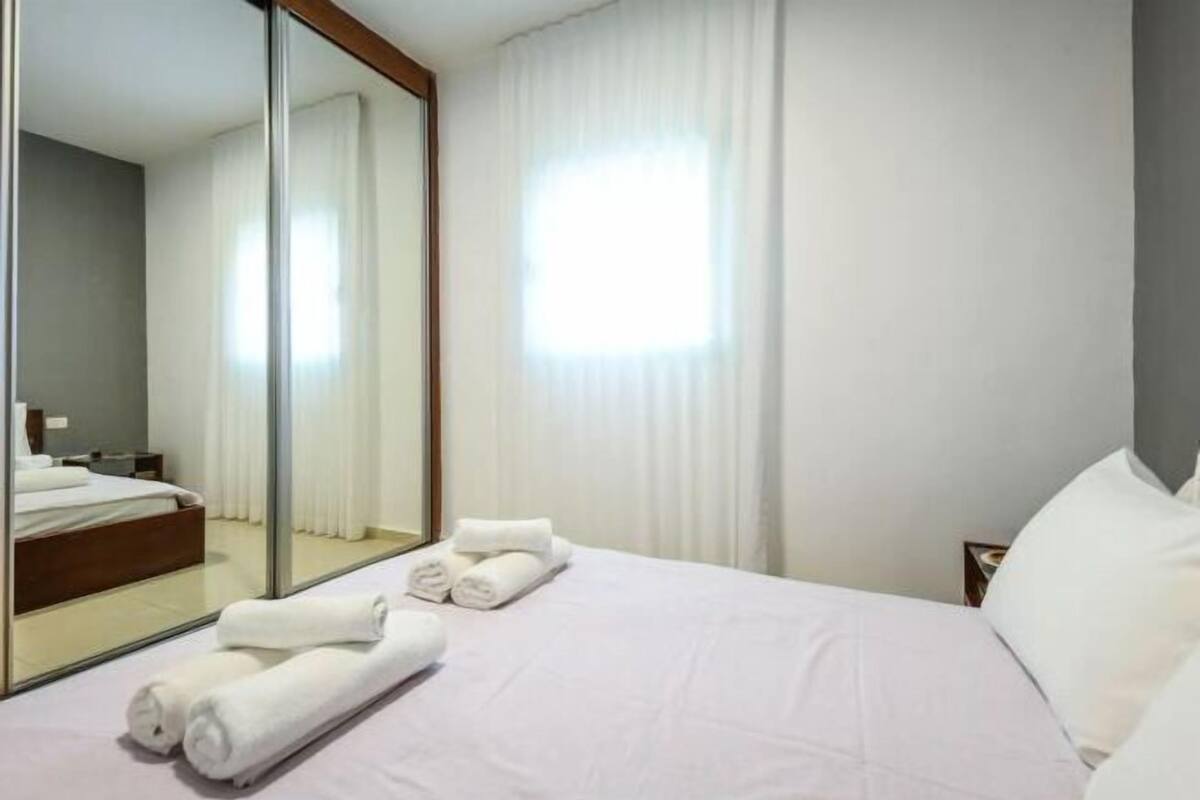 Ein Hotelzimmer mit Bett, großem Spiegel, Nachttisch und Fenster mit Vorhängen.