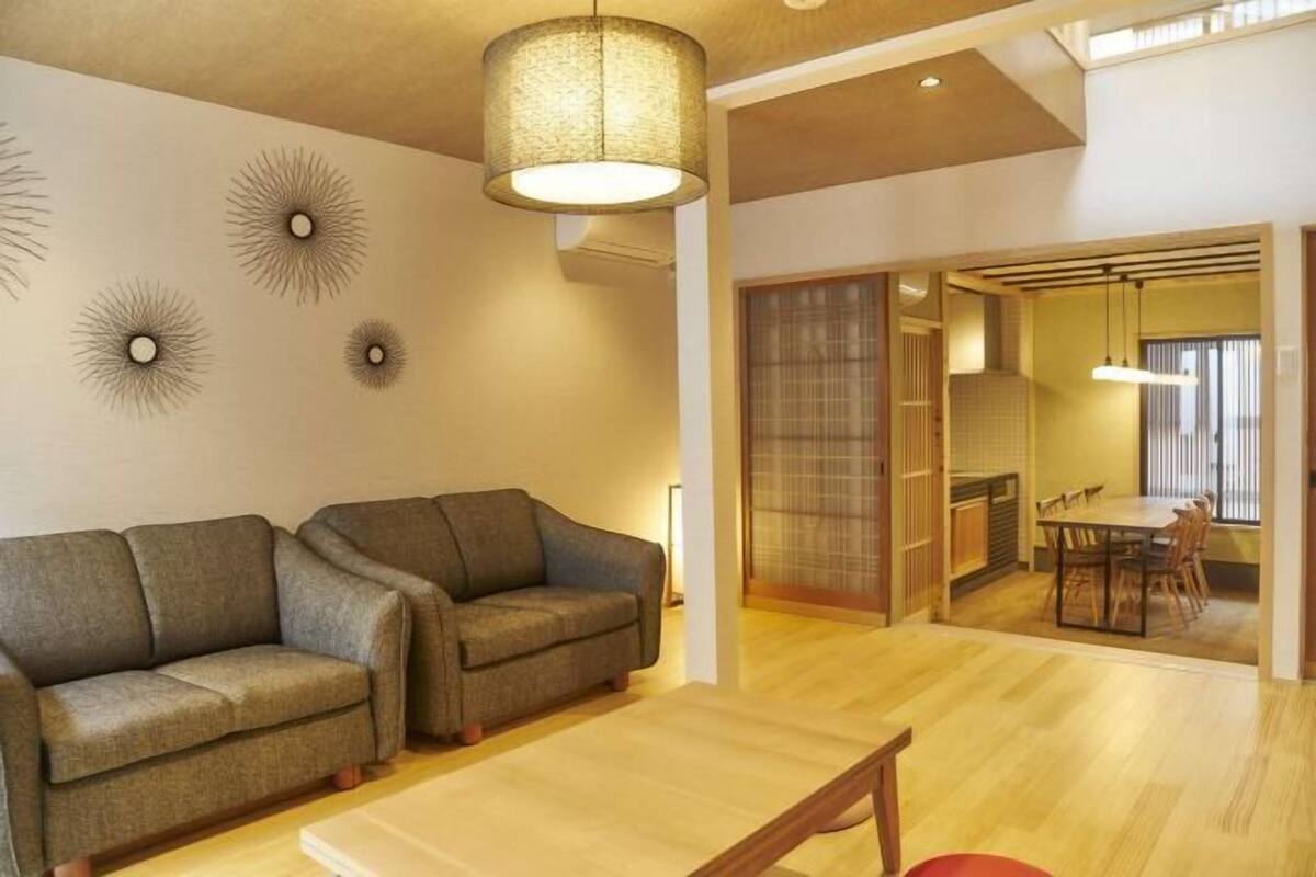 A modern living room with a sofa, a dining table, and a kitchen area visible through a sliding door.