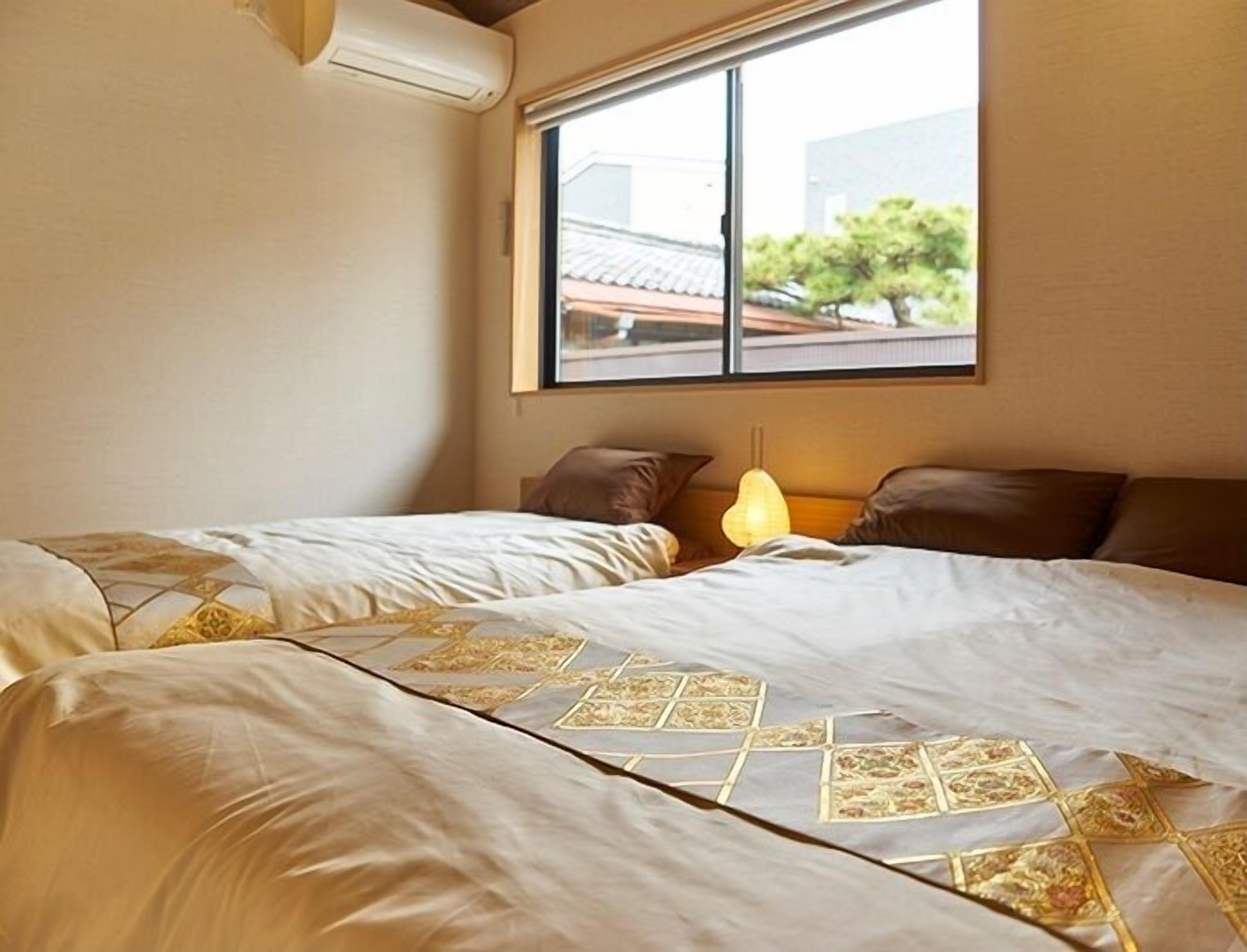 A bedroom with two beds, a window, and a wall-mounted air conditioner.