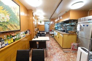 A narrow, well-lit restaurant with wooden walls and a long counter. There are several tables and chairs, a refrigerator, and a kitchen area in the background. - House TOKYO ASAKUSA (Tokyo)