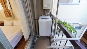 A balcony with a white air conditioning unit, a potted plant, and a view of the building's exterior. - House TOKYO ASAKUSA (Tokyo)