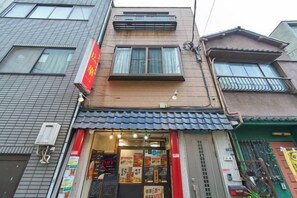 A two-story building with a ground-floor shop entrance, a visible air conditioning unit, and a small balcony on the upper floor. - House TOKYO ASAKUSA (Tokyo)