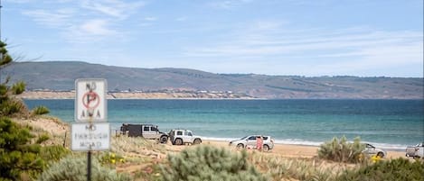 A beach with a no parking sign, vehicles parked on the sand, and a clear view of the ocean.