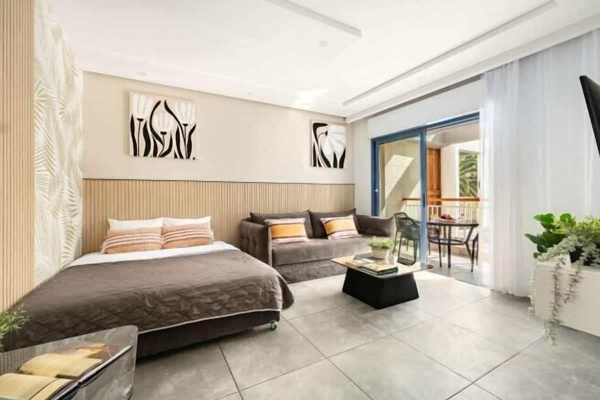 Una habitación de hotel moderna con cama, sofá y balcón con mesa y sillas.