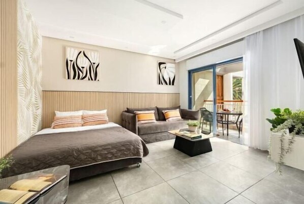 Una habitación de hotel moderna con cama, sofá y balcón con mesa y sillas.
