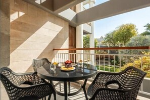 Un balcón con una mesa redonda y sillas, un pequeño conjunto de comedor y vistas a un jardín.