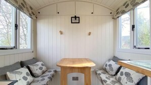 A cozy room with a wooden table, two cushioned seating areas, and a window with a view.