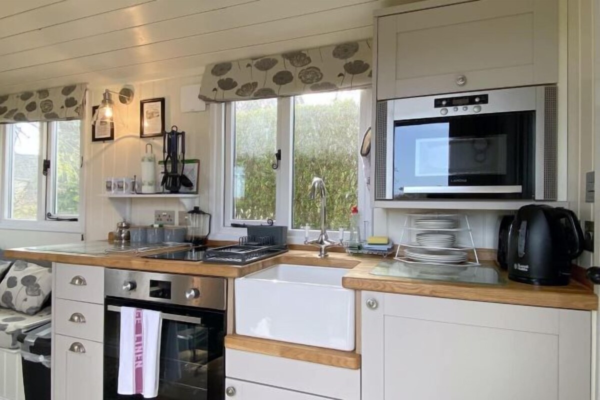 A compact kitchen with a built-in oven, microwave, and sink. There are cabinets, a countertop, and a window providing natural light.